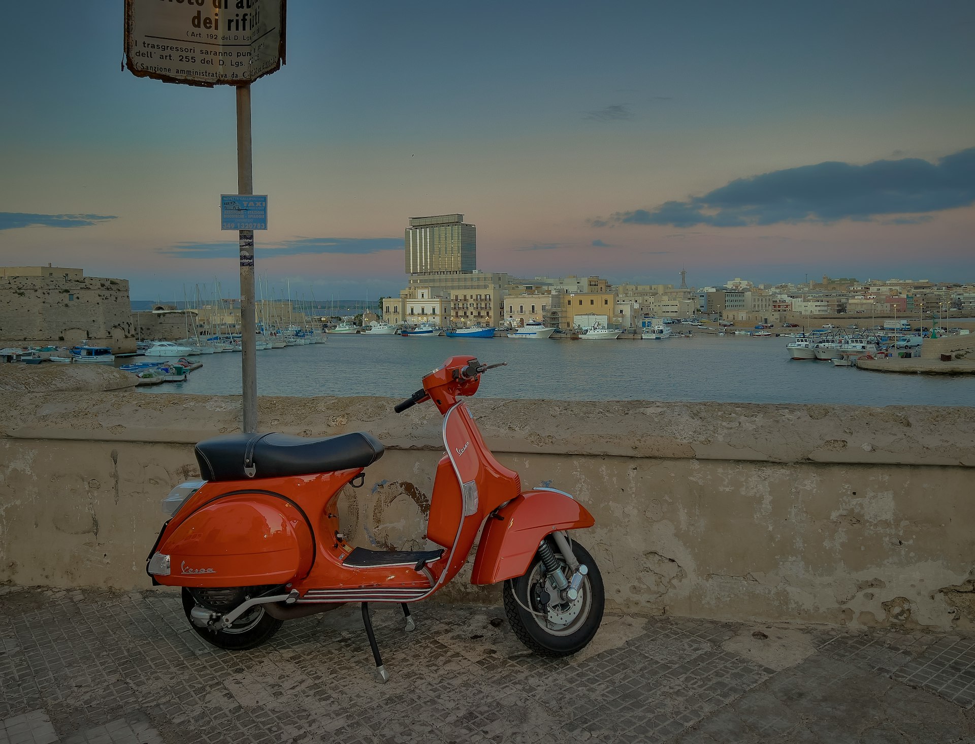 a red scooter parked next to a wall near a body of water